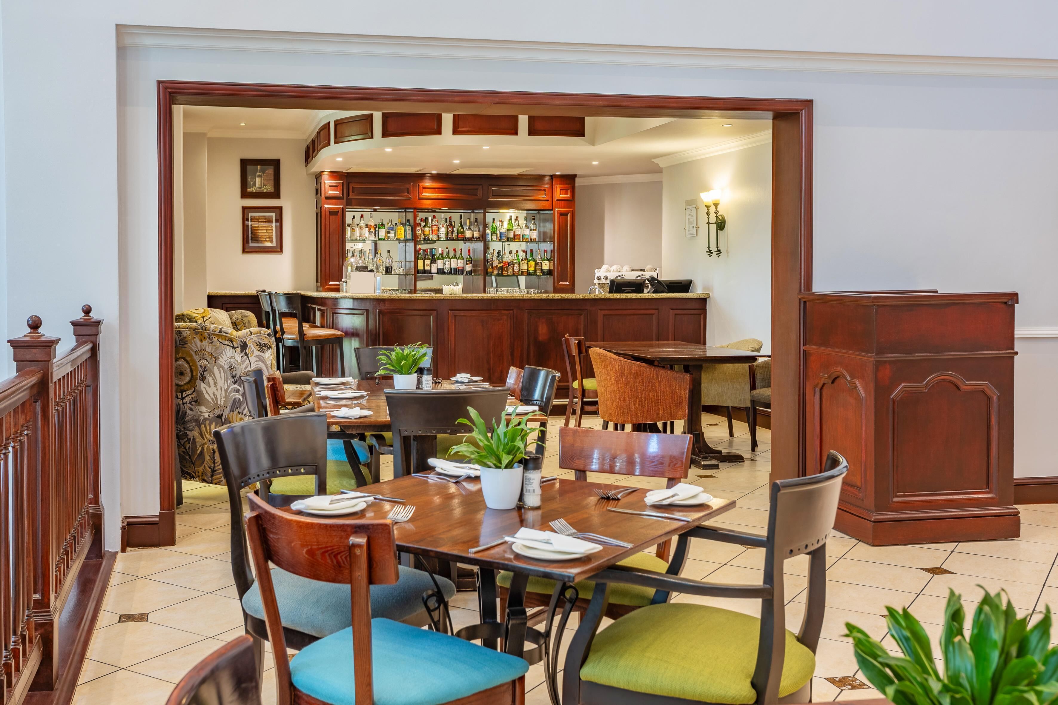 Un área de comedor con una barra al fondo, muebles de madera y una planta en maceta sobre la mesa.