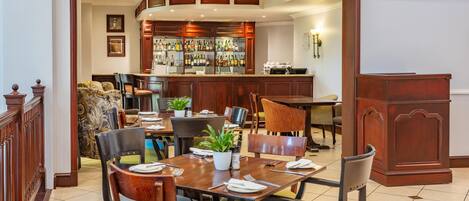 A dining area with a bar in the background, wooden furniture, and a potted plant on the table.