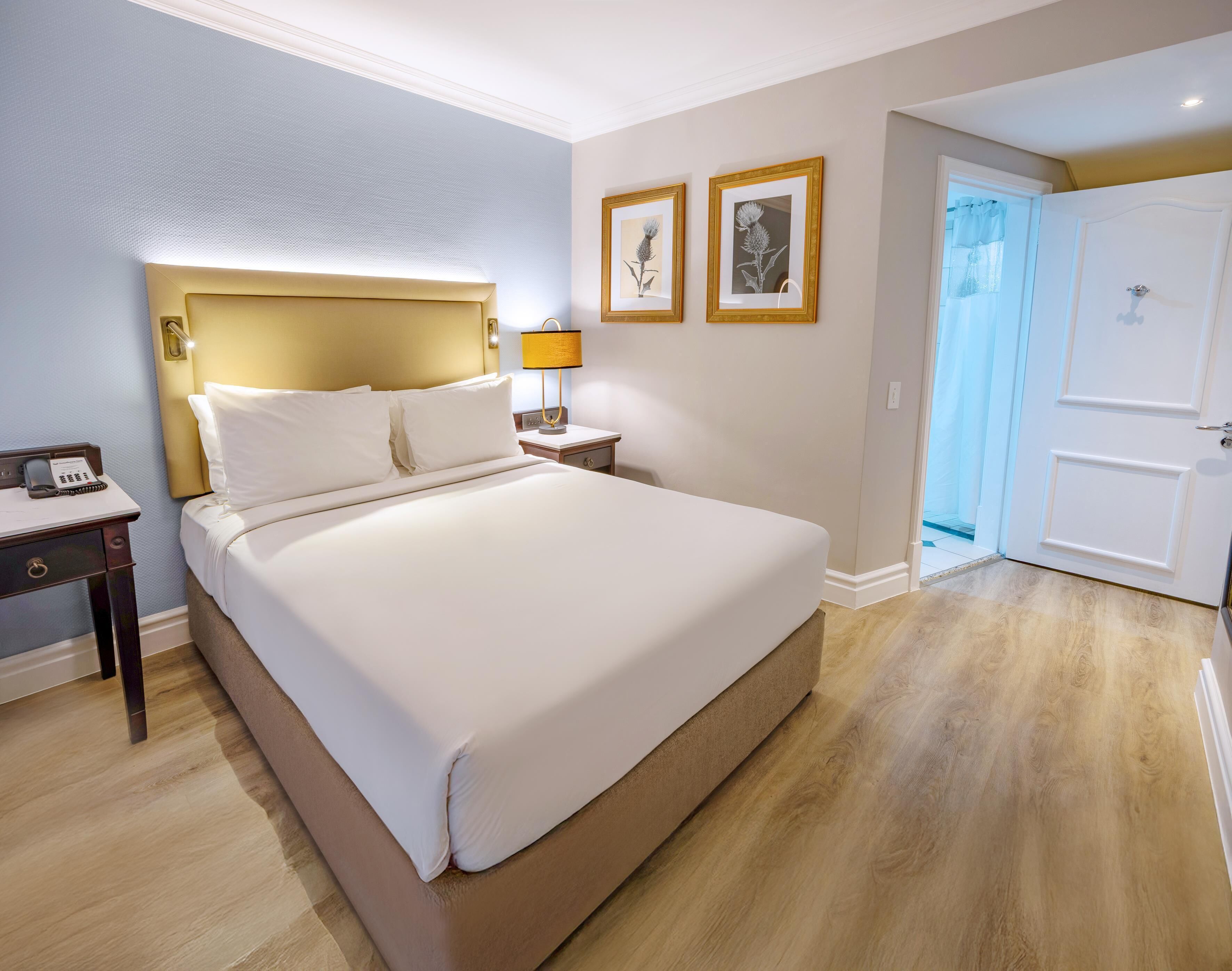 A hotel room with a large bed, bedside table with a lamp, and two framed pictures on the wall.