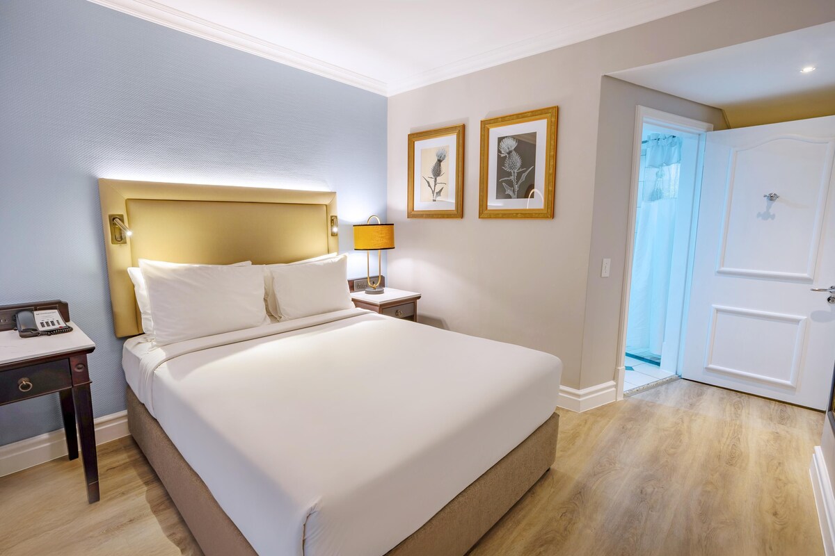 A hotel room with a large bed, bedside table with a lamp, and two framed pictures on the wall.