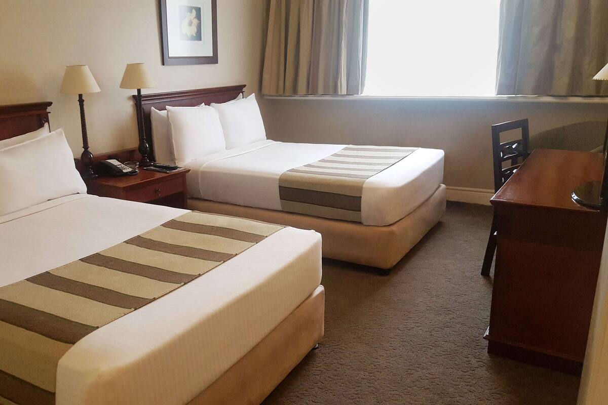 A hotel room with two beds, a desk, a chair, and a window with curtains.