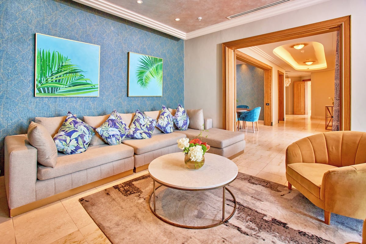 Una sala moderna con un sofá beige, una mesa redonda de centro y un sillón azul.