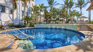 Una piscina con borde de azulejos, sillas de descanso y palmeras.