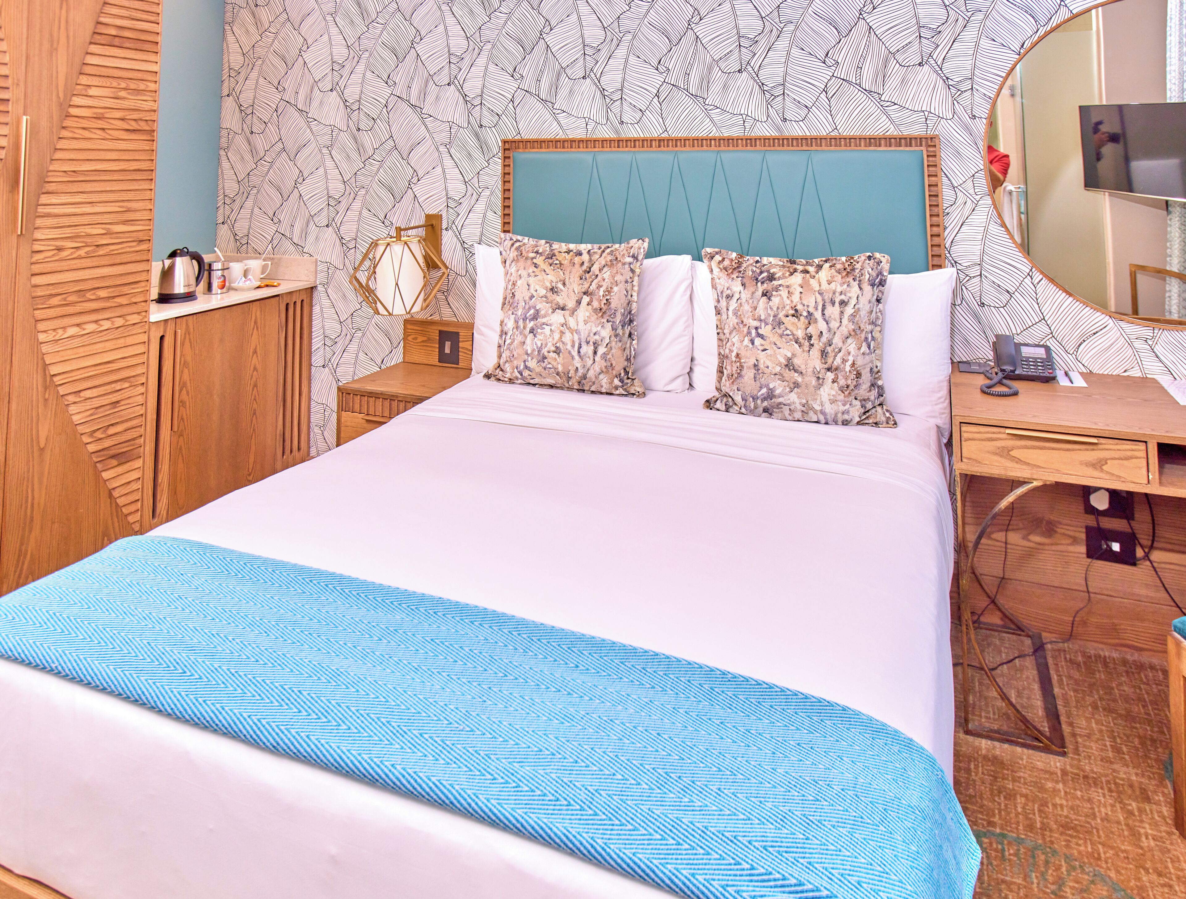 Une chambre d’hôtel avec un grand lit, une commode en bois, un bureau avec un téléphone et un miroir.