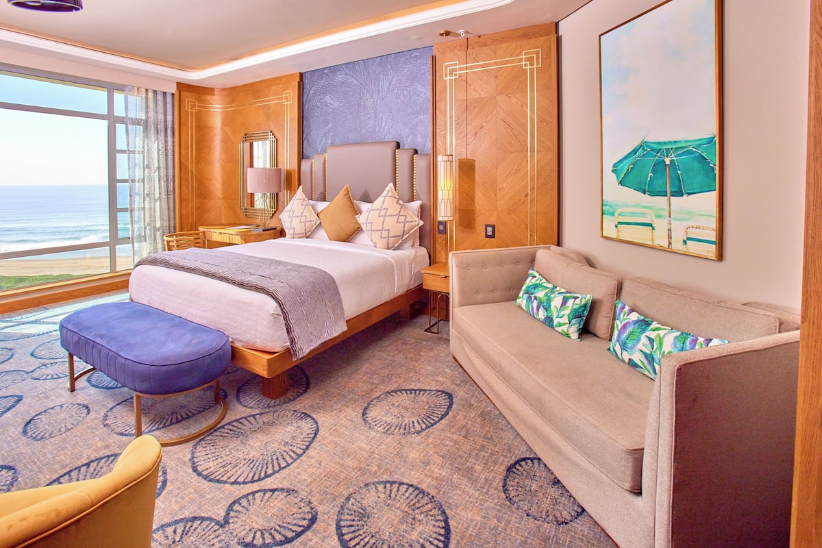 Habitación de hotel con una cama grande, un sofá, una mesita y vista al océano.