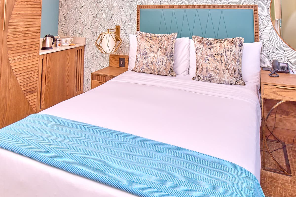 Una cama bien hecha con colcha azul y blanca, cabecera de madera y almohadas estampadas.