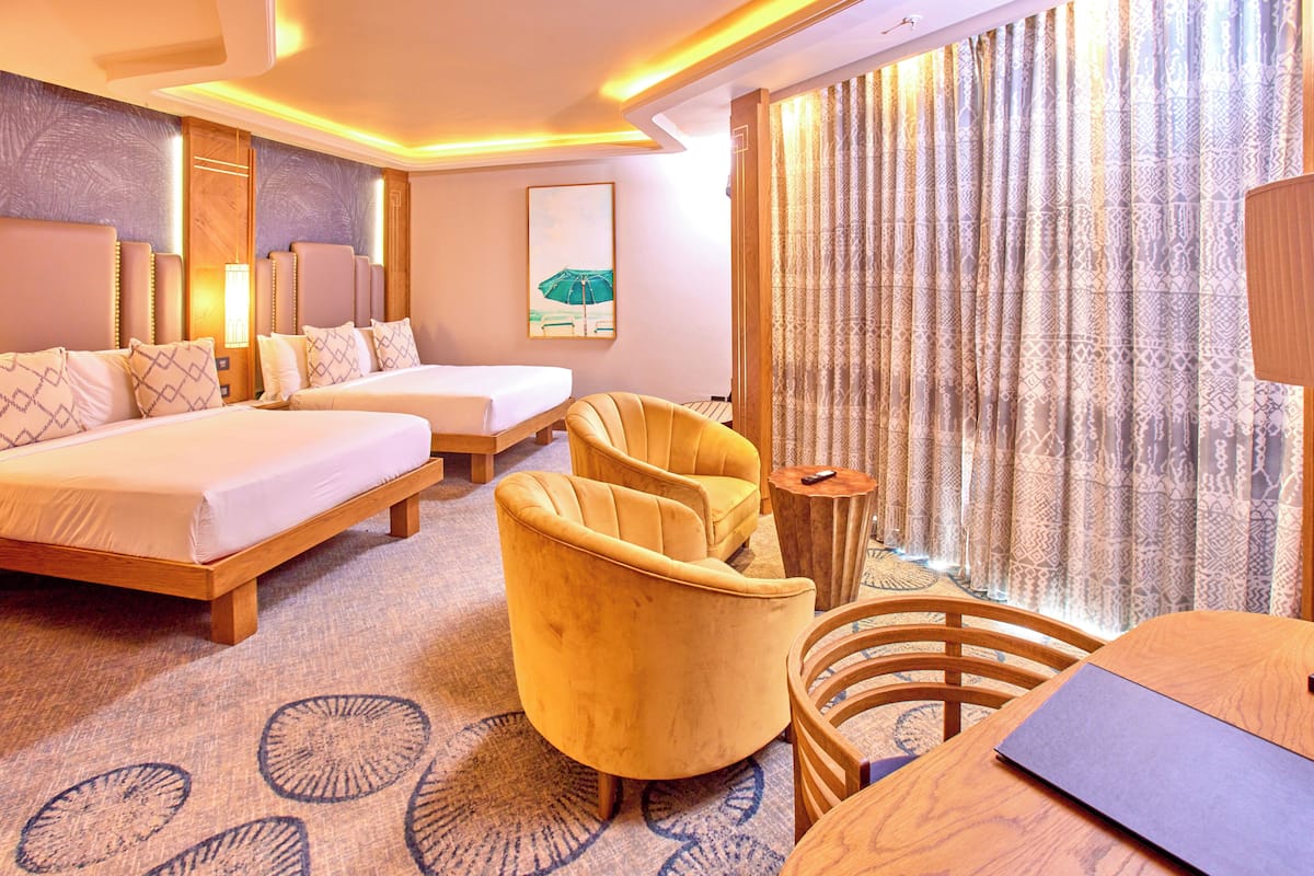 Habitación de hotel con cama, dos sillones, una mesita de madera y un ventanal con cortinas estampadas.