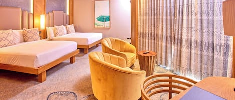 A hotel room with a bed, two armchairs, a small wooden table, and a large window with patterned curtains.