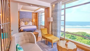 Habitación de hotel con cama, sofá, sillón, una mesita y vista a la playa.