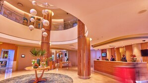 Un vestíbulo espacioso con una recepción, un gran tapete decorativo y una escalera que conduce a un nivel superior.