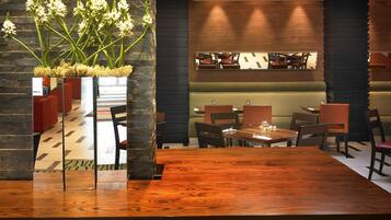 Un restaurante con mesa y sillas de madera, un pilar de piedra con flores y una zona de estar con mostrador.