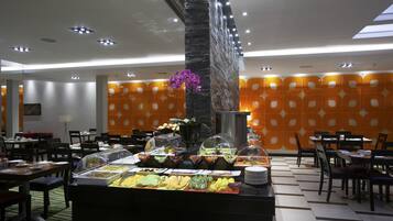 Zona de bufé con diversos alimentos, un pilar decorativo y paredes con estampado anaranjado.