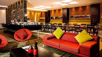 A hotel lobby with a bar area, red sofas, and a stone wall.