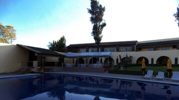 A swimming pool with a reflection of a building and trees. There are outdoor seating areas with umbrellas.