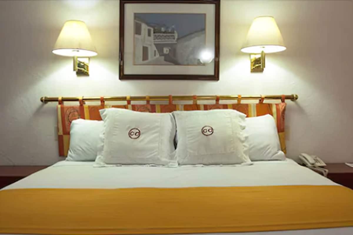Een hotelkamer met een bed, twee bedlampen, een ingelijst schilderij aan de muur en een telefoon op het nachtkastje.