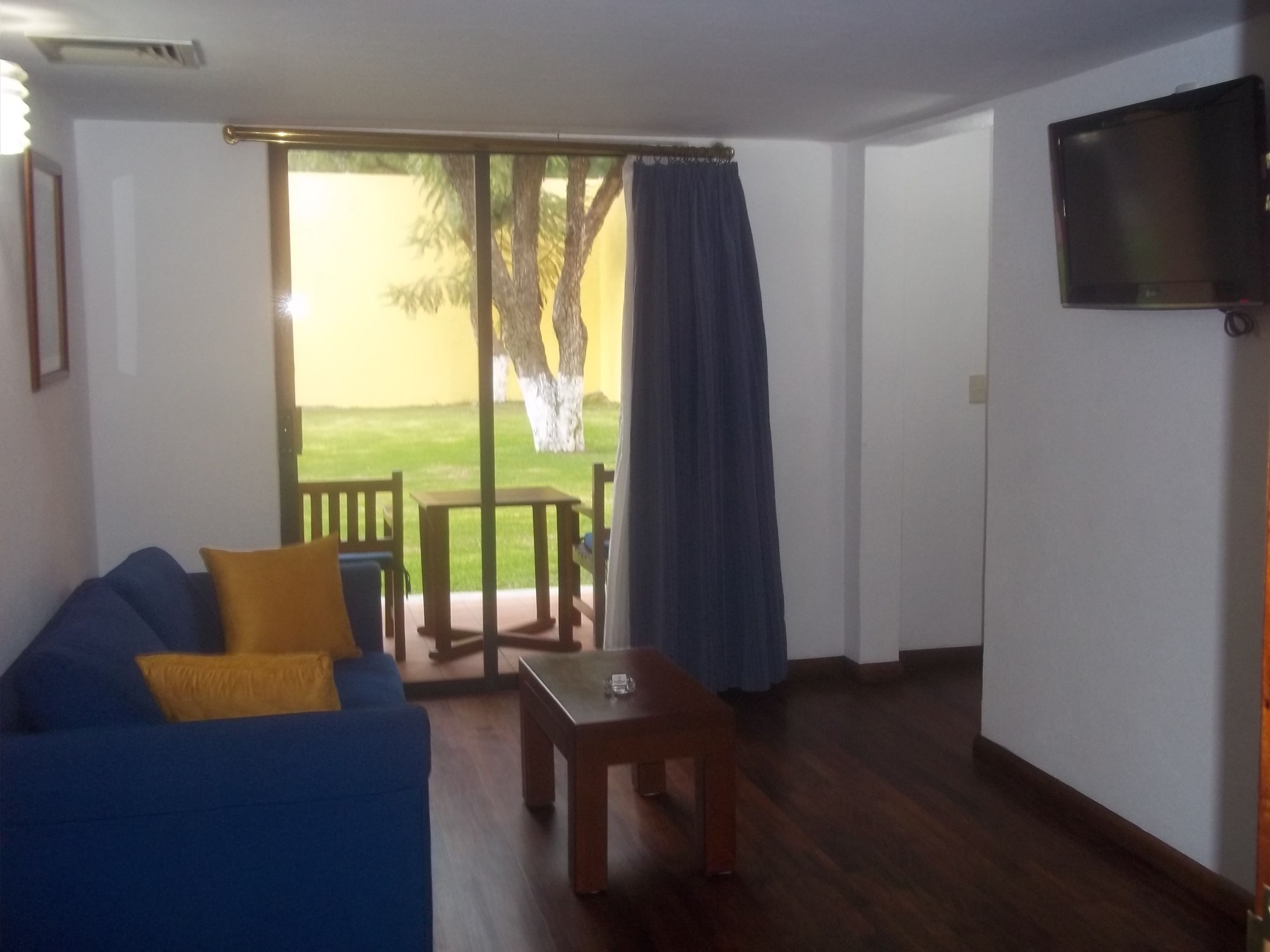 A room with a blue sofa, a small wooden table, and a TV mounted on the wall.