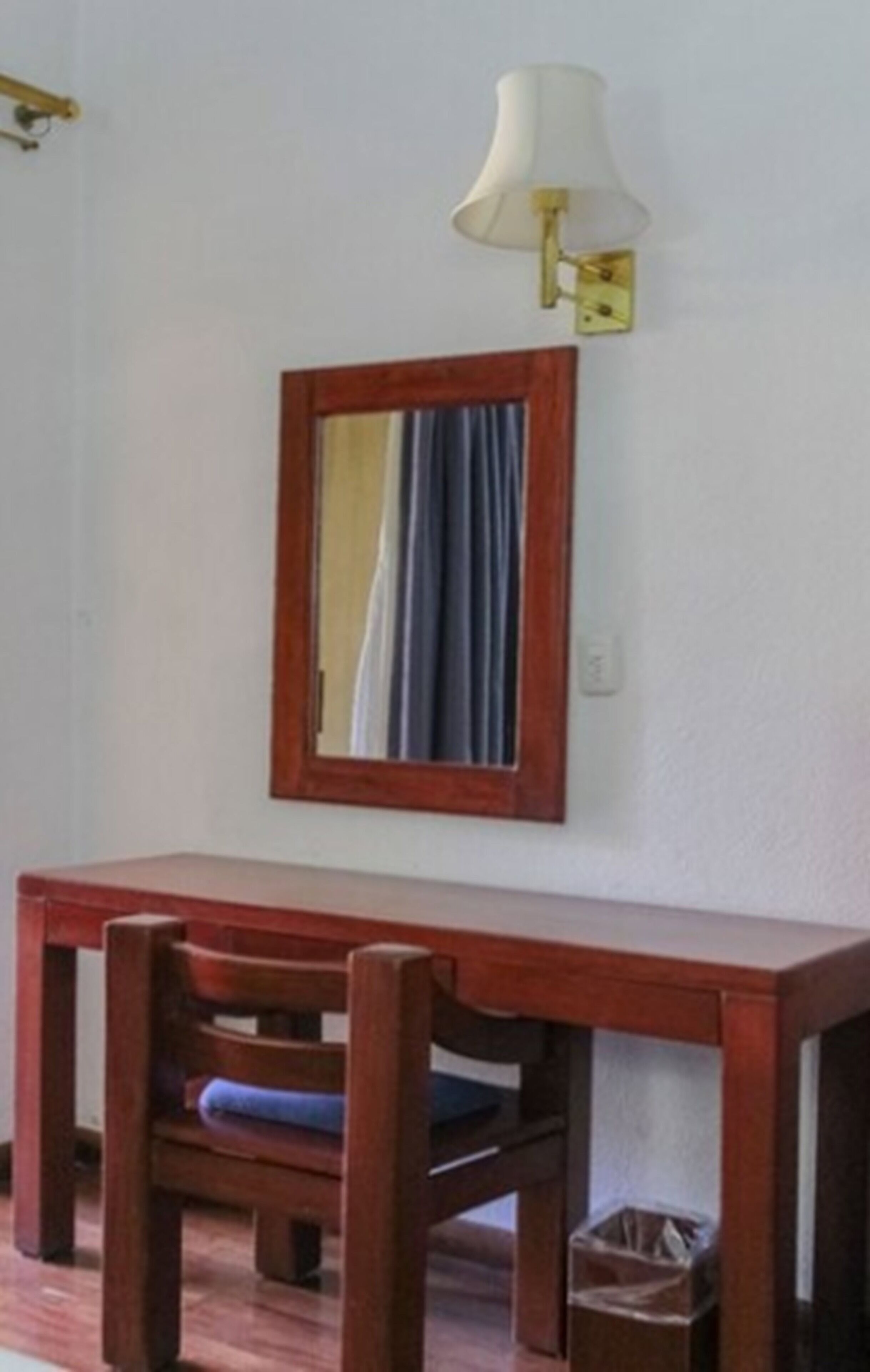 A wooden desk with a chair, a wall-mounted lamp, and a mirror.