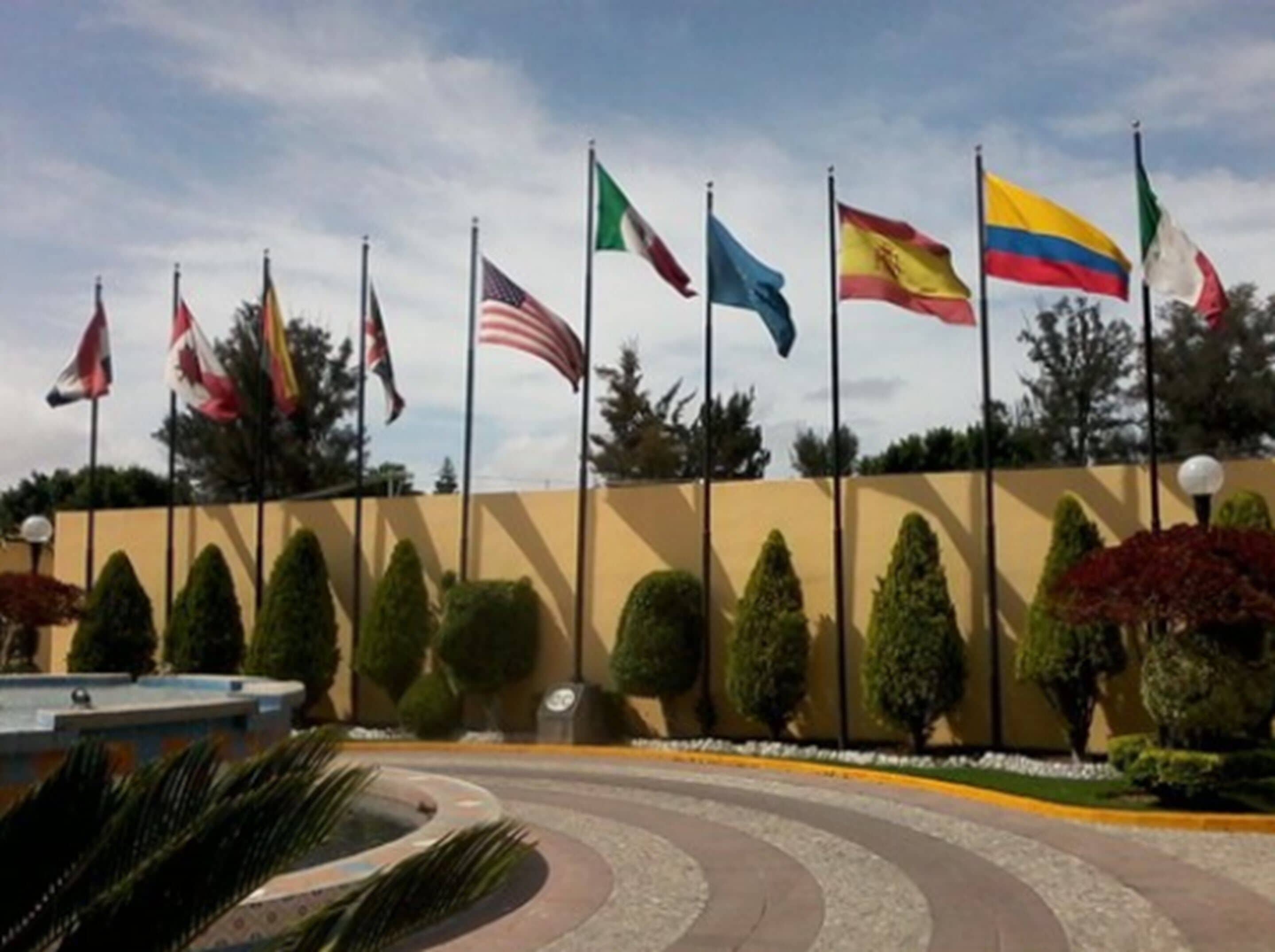 A building with multiple national flags displayed outside, surrounded by well-maintained landscaping and a curved pathway.