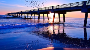A pier extending into the ocean at sunset with birds flying above. - Holiday Inn Express Jacksonville Beach by IHG (Jacksonville Beach)