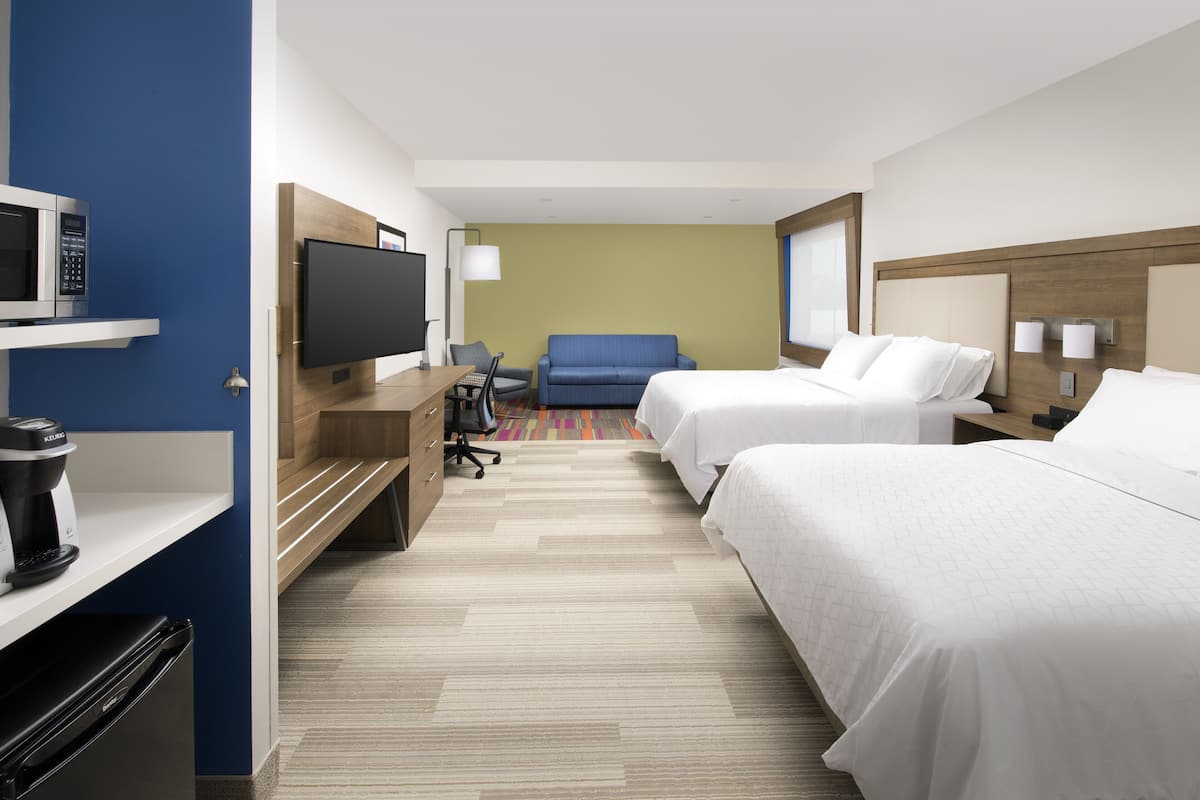 A hotel room with two beds, a television, a desk with a coffee maker, and a microwave.