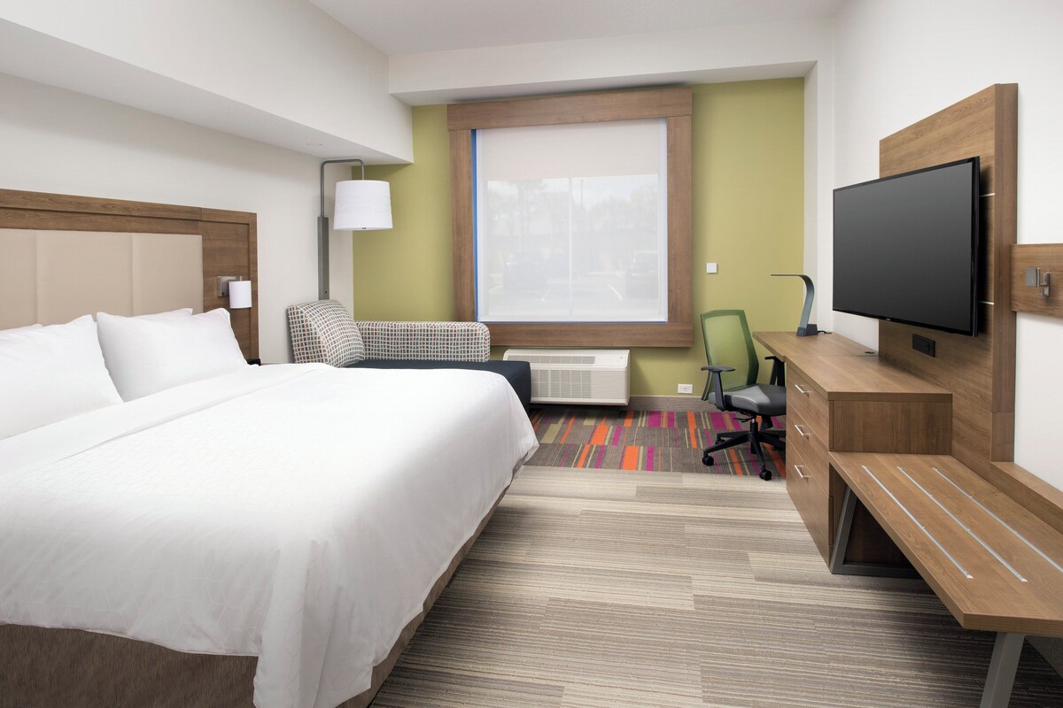Quarto de hotel com cama, escrivaninha, cadeira, televisão e janela.