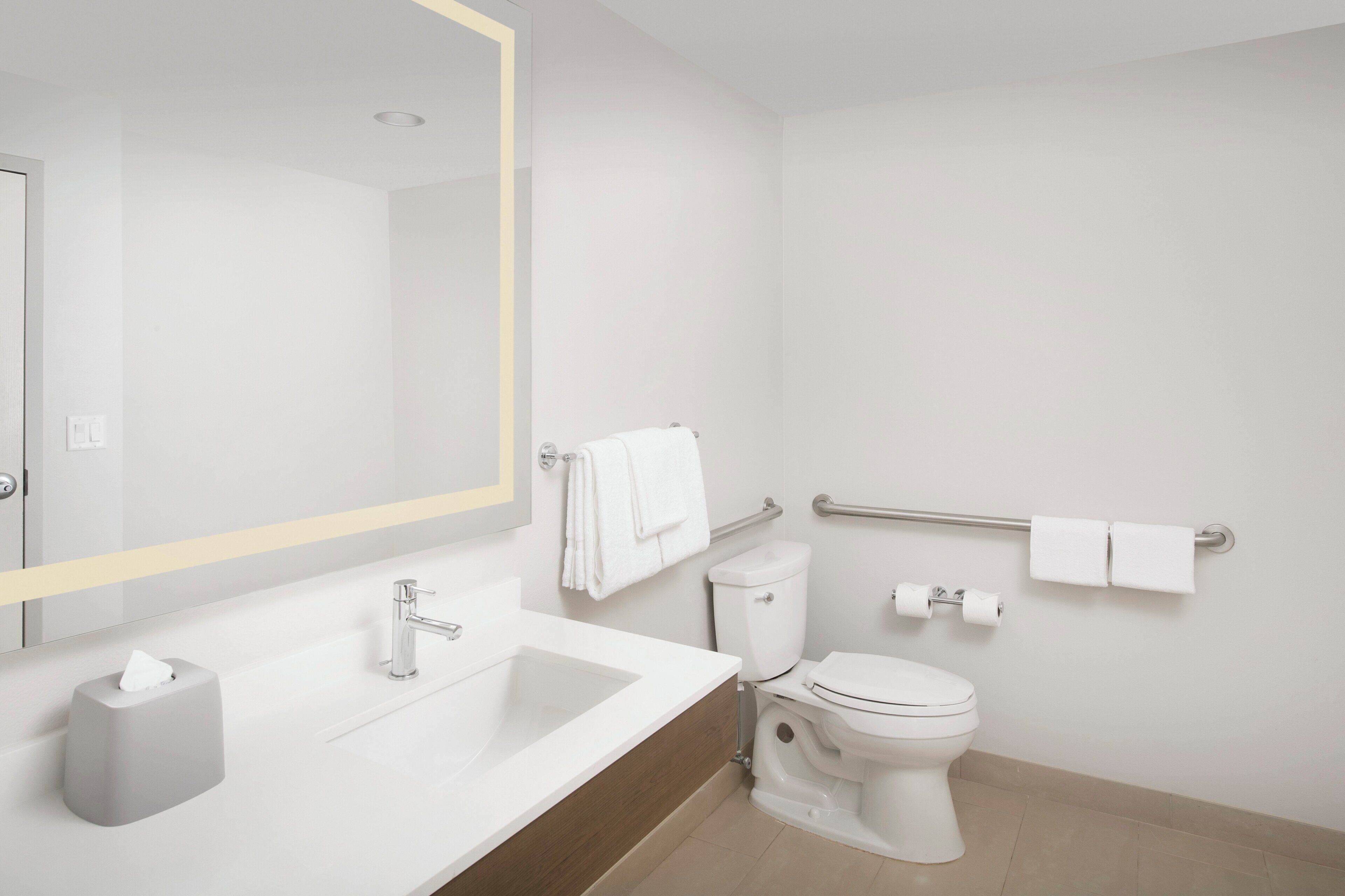 Ein modernes Badezimmer mit Waschbecken, Spiegel, Toilette und Handlauf.