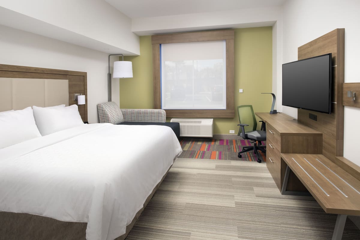 A hotel room with a bed, desk, chair, television, and window.