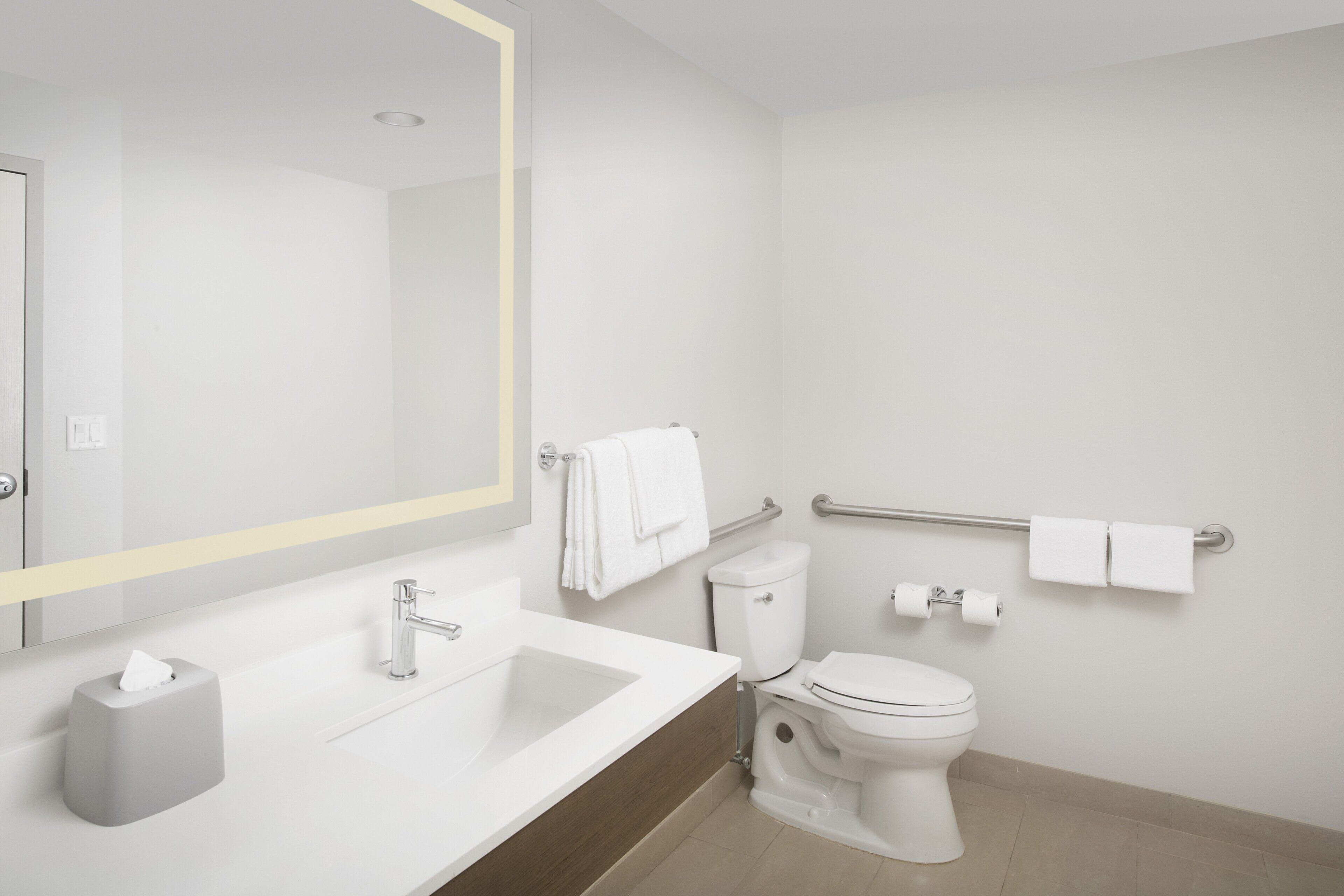 A modern bathroom with a white sink, mirror, toilet, and handrails.