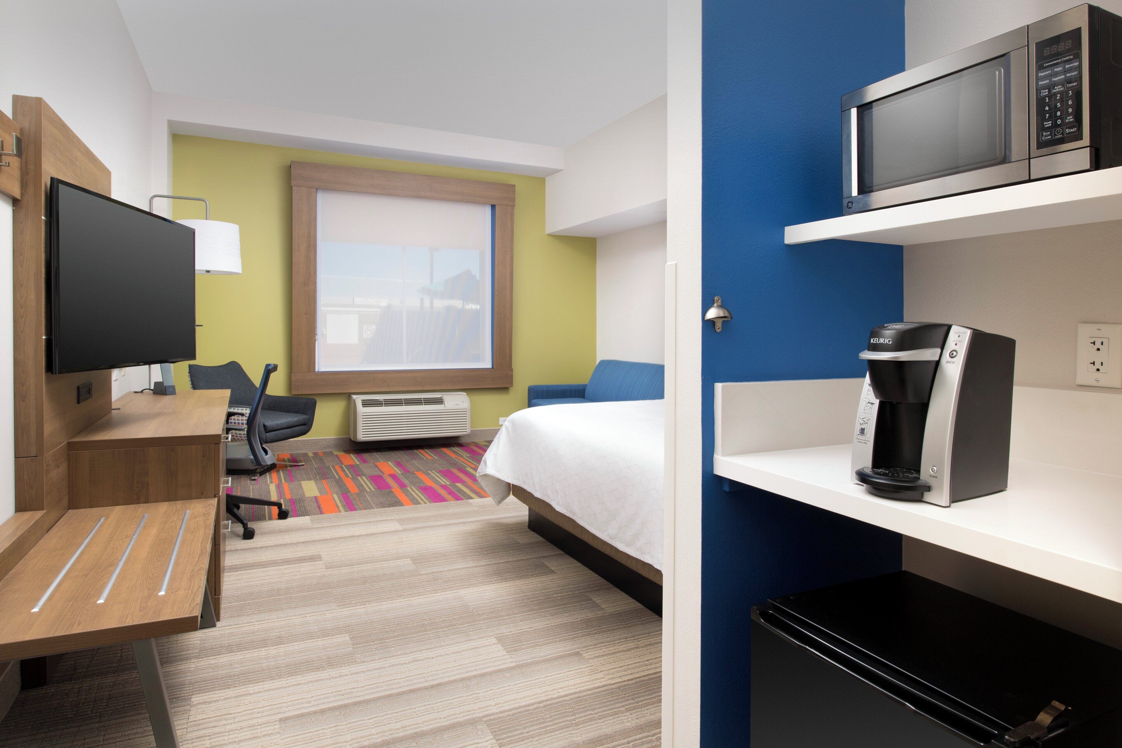 A hotel room with a bed, a desk with a chair, a television, a microwave, and a coffee maker.