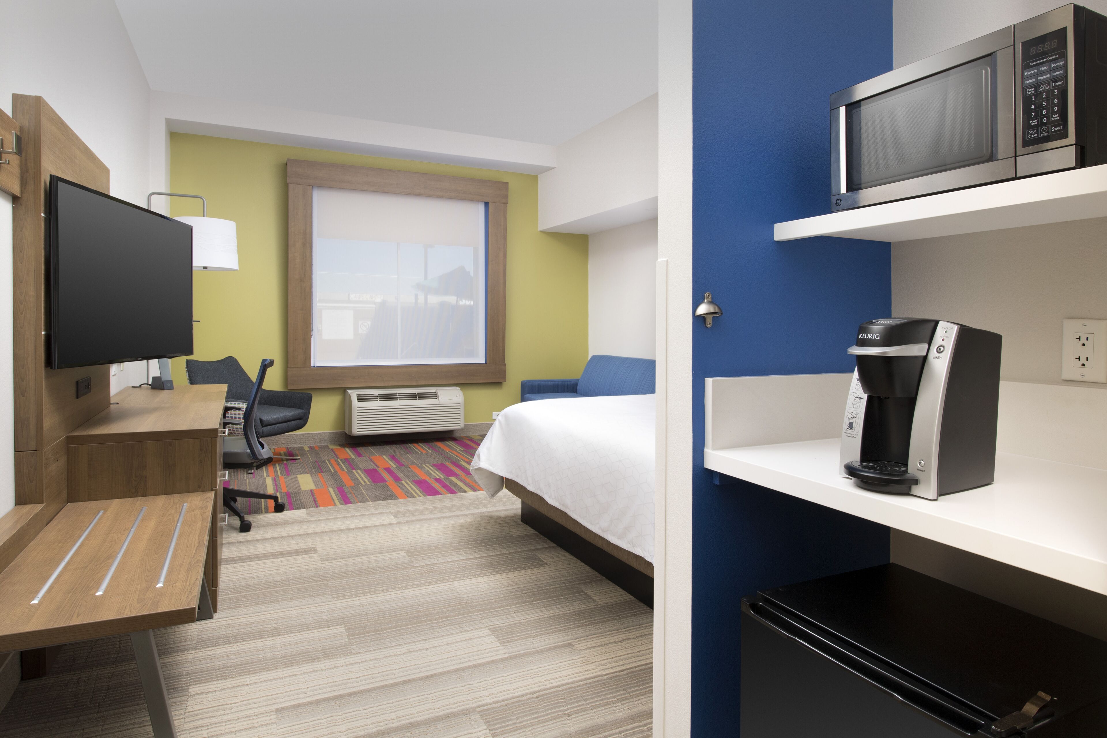 A hotel room with a bed, a desk, a television, a coffee maker, and a microwave.