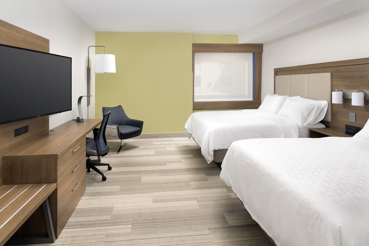 A hotel room with two beds, a desk with a chair, a television, and a window.