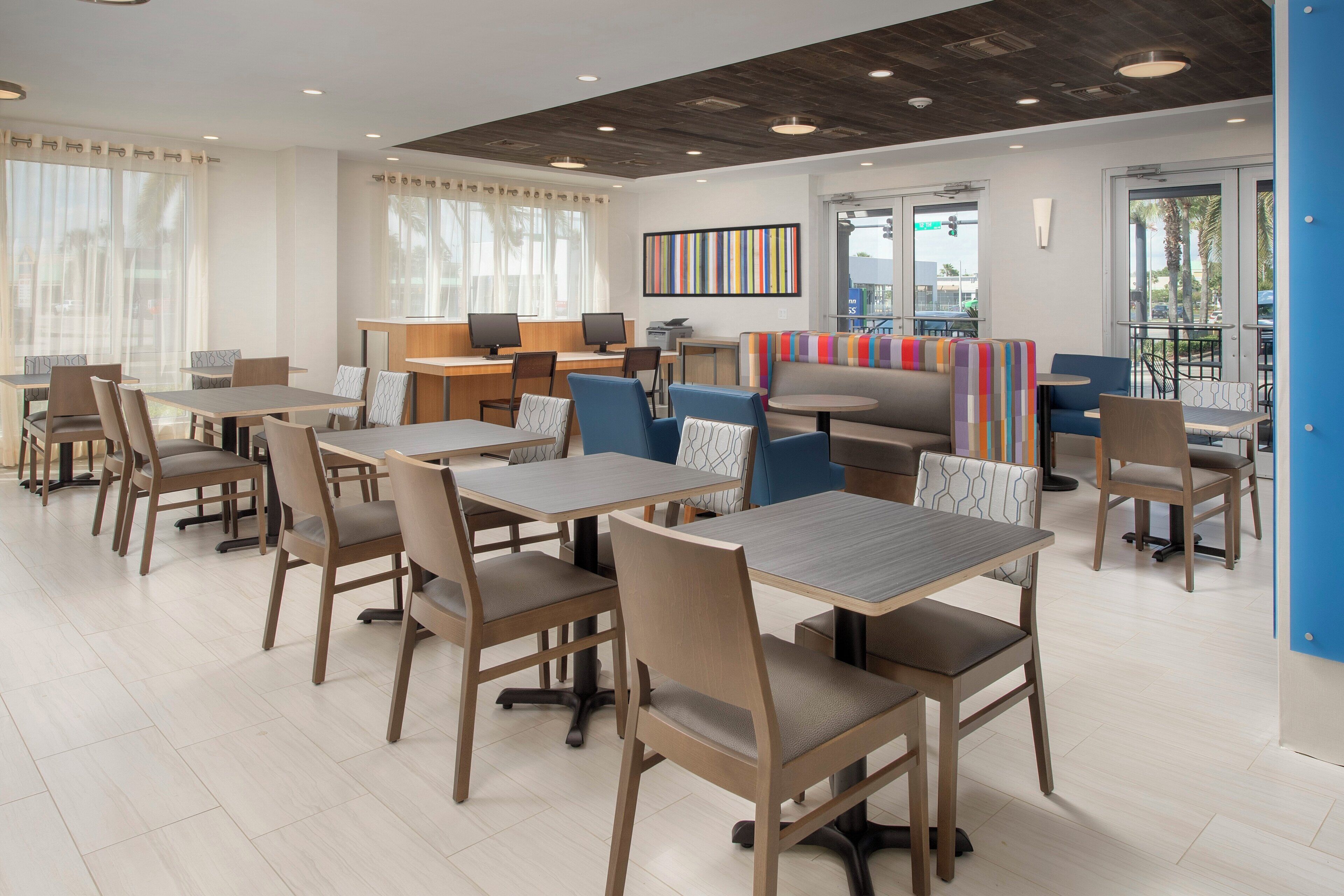 A modern dining area with multiple tables and chairs, a counter with computers, and a colorful wall art piece.