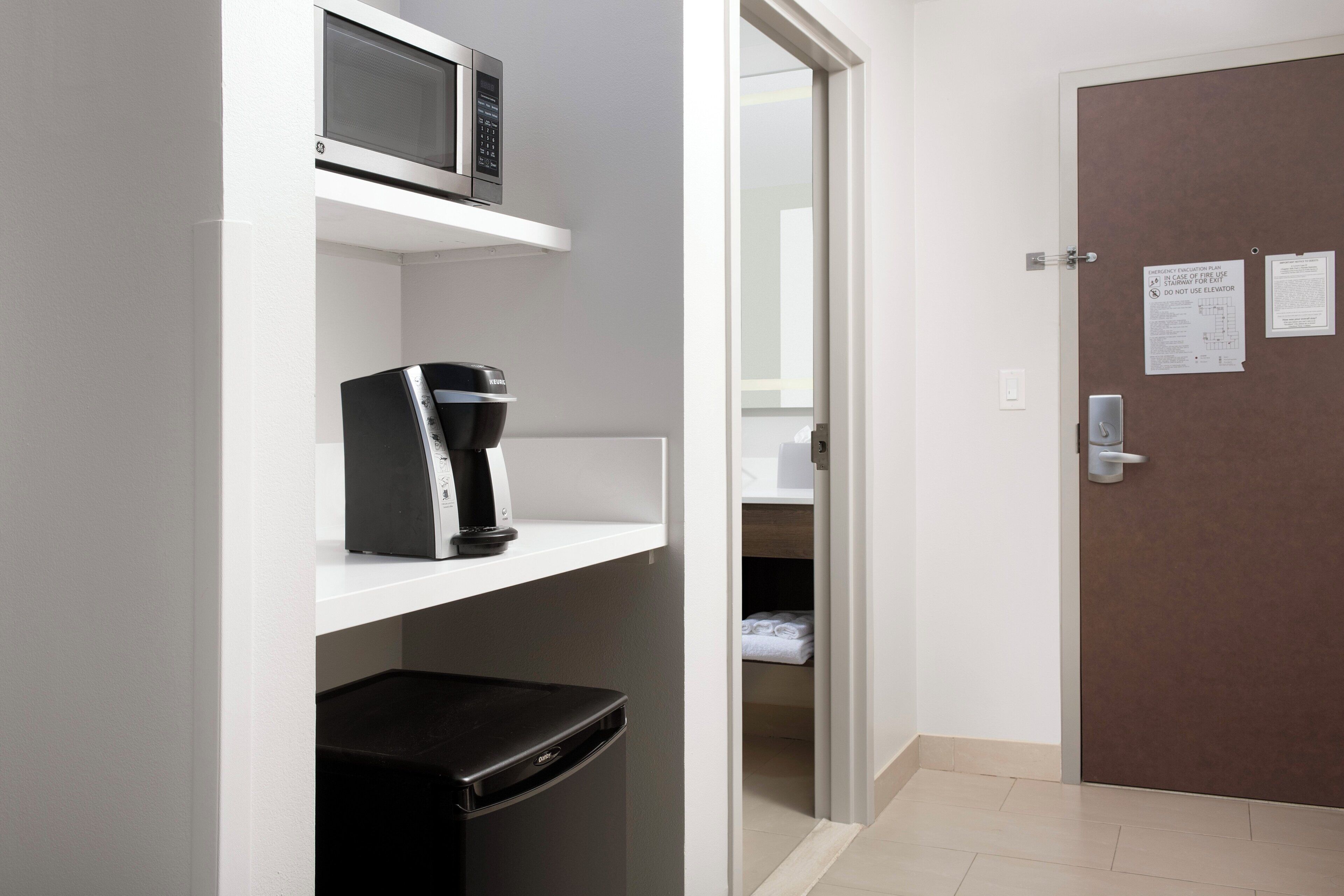 Habitación de hotel compacta con microondas, cafetera y refrigerador en la pared.