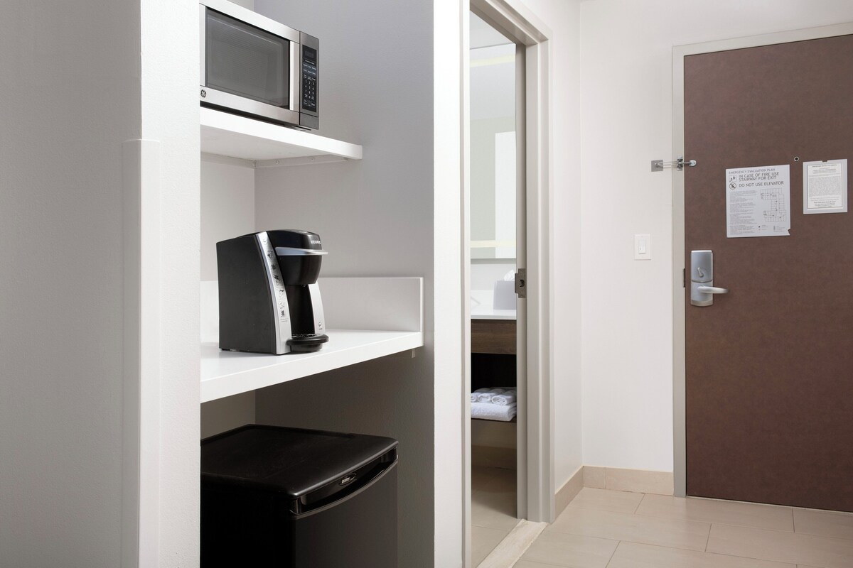 Quarto de hotel compacto com micro-ondas, cafeteira e frigorífico na parede.