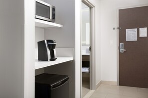 Quarto de hotel com micro-ondas, cafeteira e frigorífico na bancada. Porta visível com um sinal e um porta-toalhas.