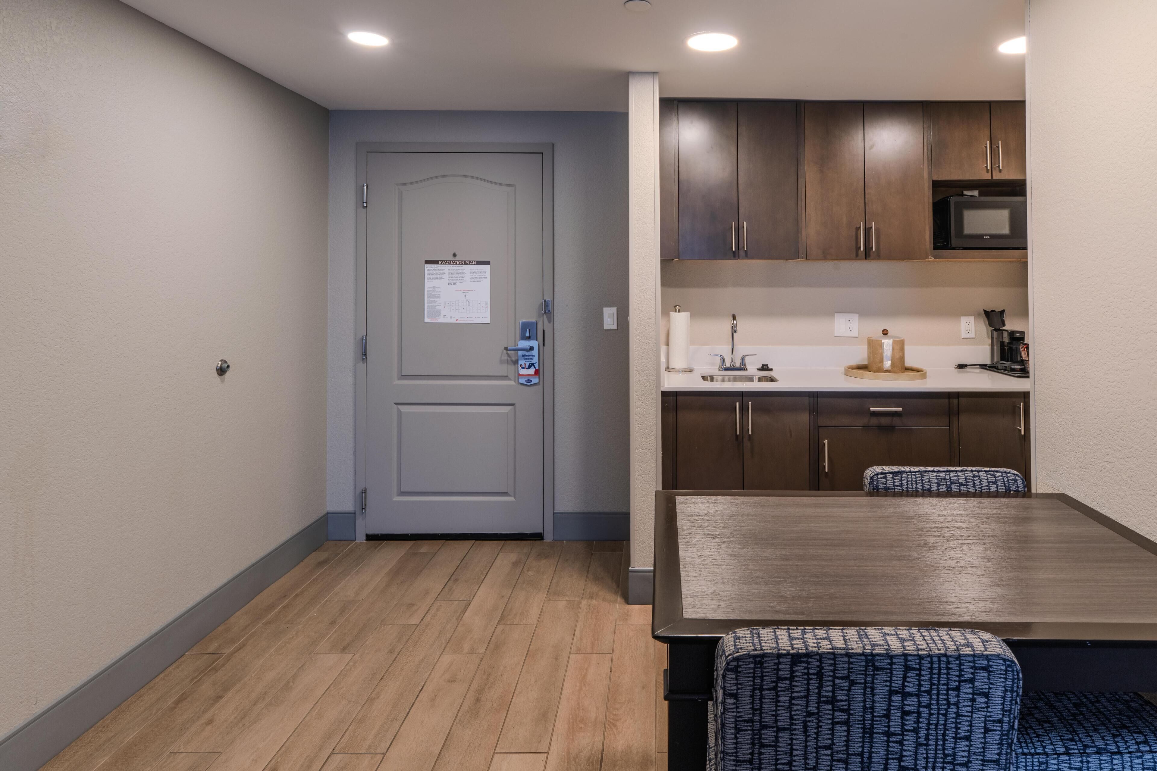 Cocina compacta con armarios de madera, un microondas y una mesa de comedor con sillas tapizadas en azul.