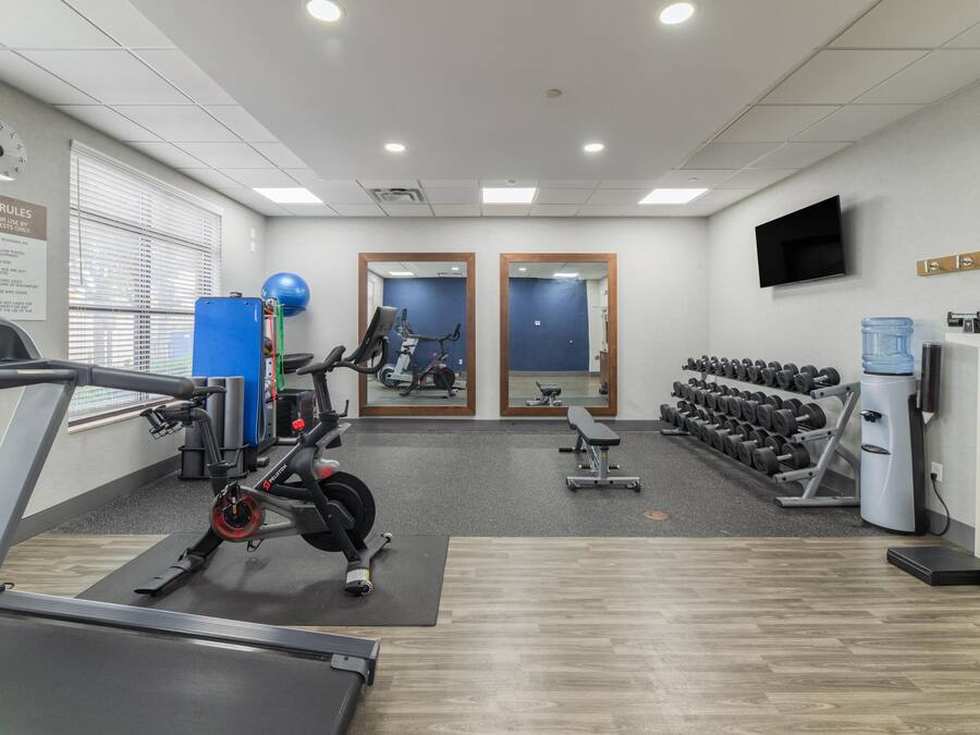 Un gimnasio con equipo de cardio, máquinas de pesas, una banca y un televisor montado en la pared.
