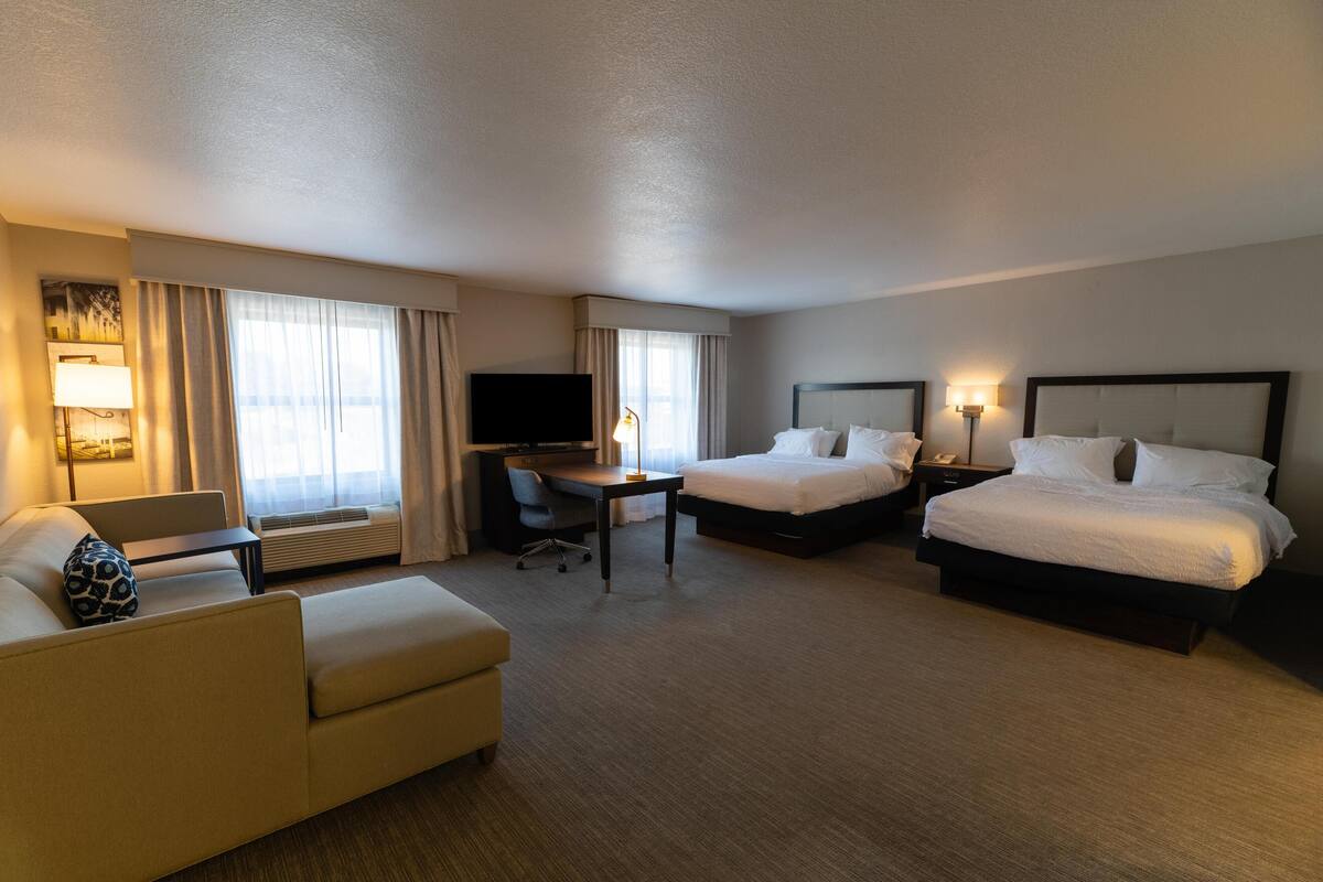 A hotel room with two beds, a desk, a chair, a sofa, and a TV.