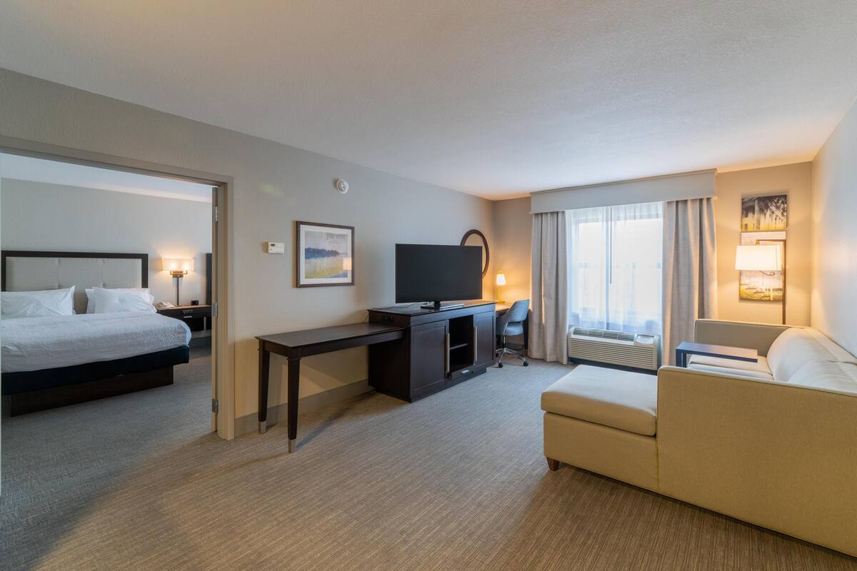 A hotel room with a bed, a desk, a television, a sofa, and a window with curtains.