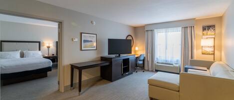 Habitación de hotel con cama, escritorio, televisor, sofá y ventana con cortinas.