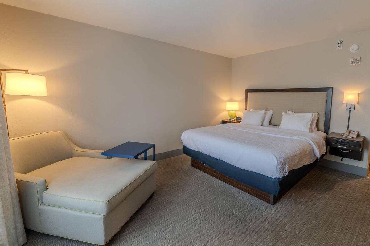 A hotel room with a bed, a small bedside table, a chair, and a lamp.