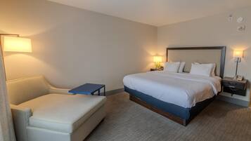 A hotel room with a bed, a small bedside table, a chair, and a lamp.