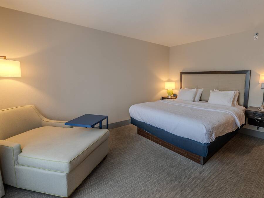 A hotel room with a bed, a small bedside table, a chair, and a lamp.