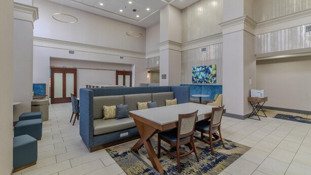 A spacious lobby with a blue sofa, a wooden table, and chairs. There is a TV on a stand and a painting on the wall. - Hampton Inn & Suites Florence-Downtown (Florence)