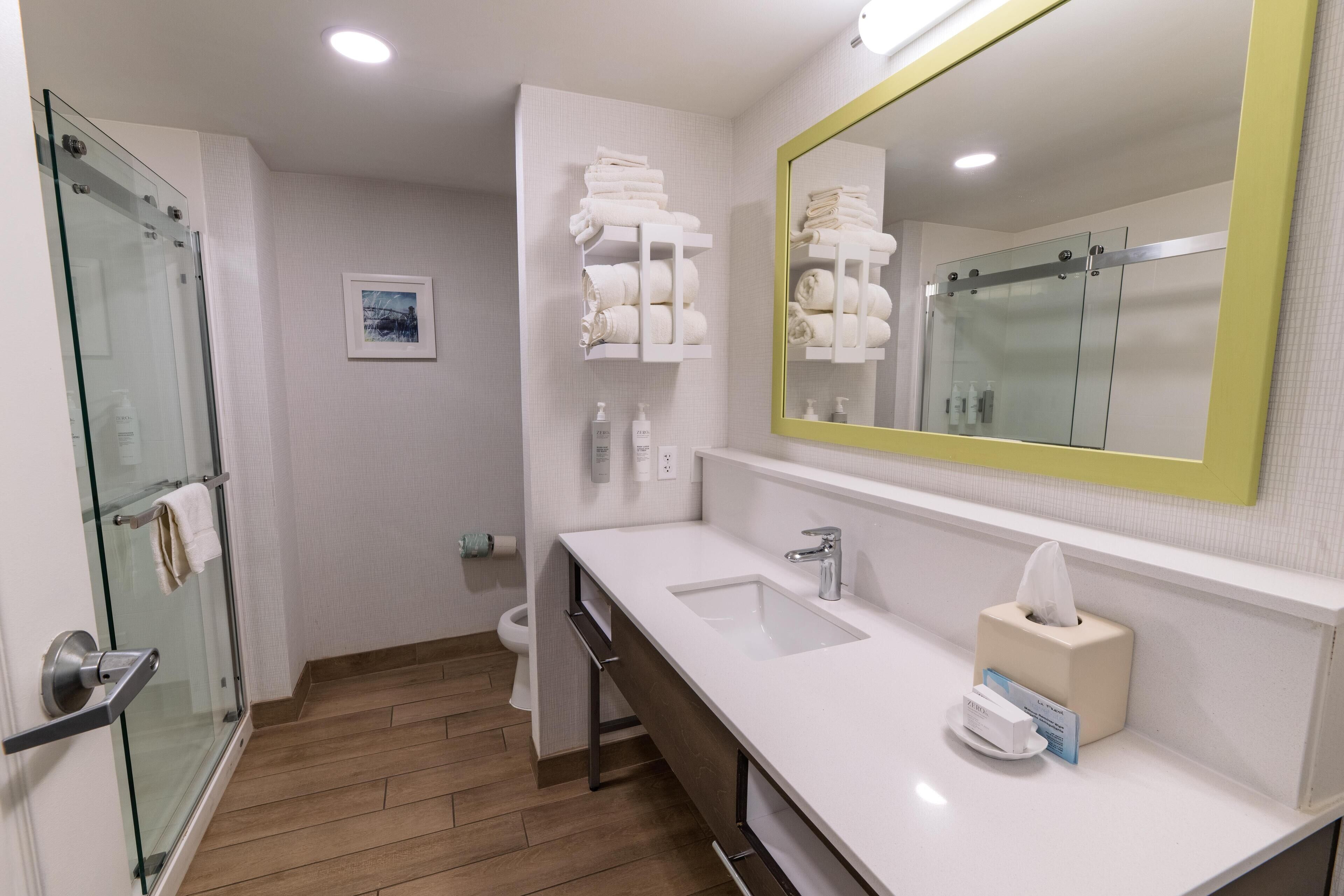 A modern bathroom with a glass shower enclosure, a white sink with a mirror, and a towel rack.