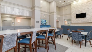 A modern dining area with a long table, blue cushioned chairs, and a stone accent wall. - Hampton Inn & Suites Florence-Downtown (Florence)