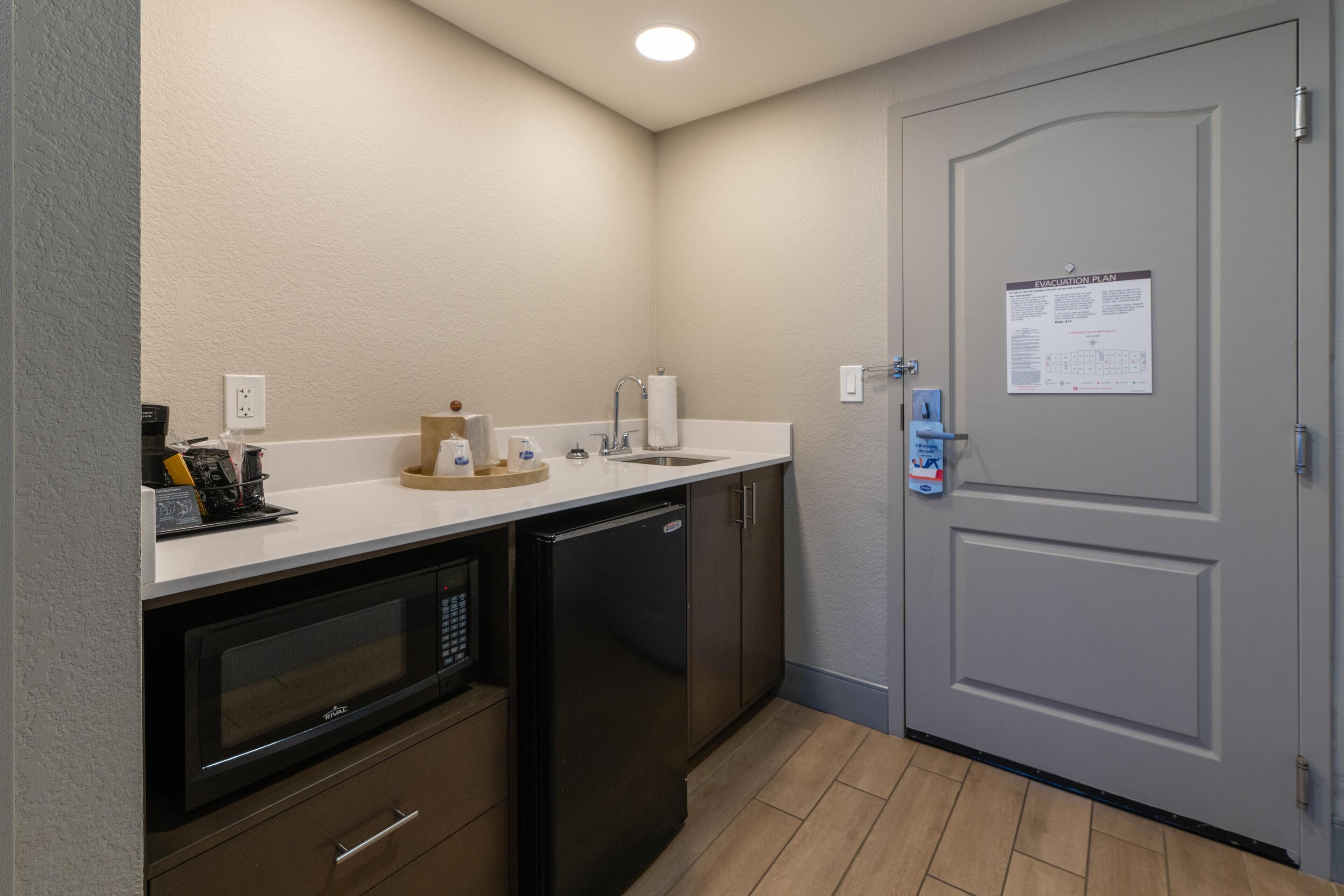 A compact kitchen with a microwave, dishwasher, and sink. A door with an evacuation plan poster is visible.