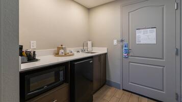 A compact kitchen with a microwave, dishwasher, and sink. A door with an evacuation plan poster is visible.