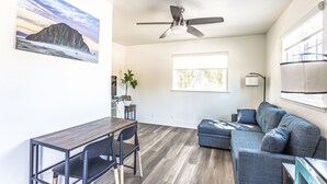 A modern living room with a dining area, a ceiling fan, and a large window providing natural light. - Coastal Breeze Inn (Morro Bay)