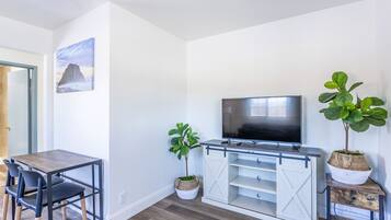 Uma sala de estar moderna com uma mesa de jantar de madeira, duas cadeiras, uma televisão de tela plana e duas plantas em vasos.